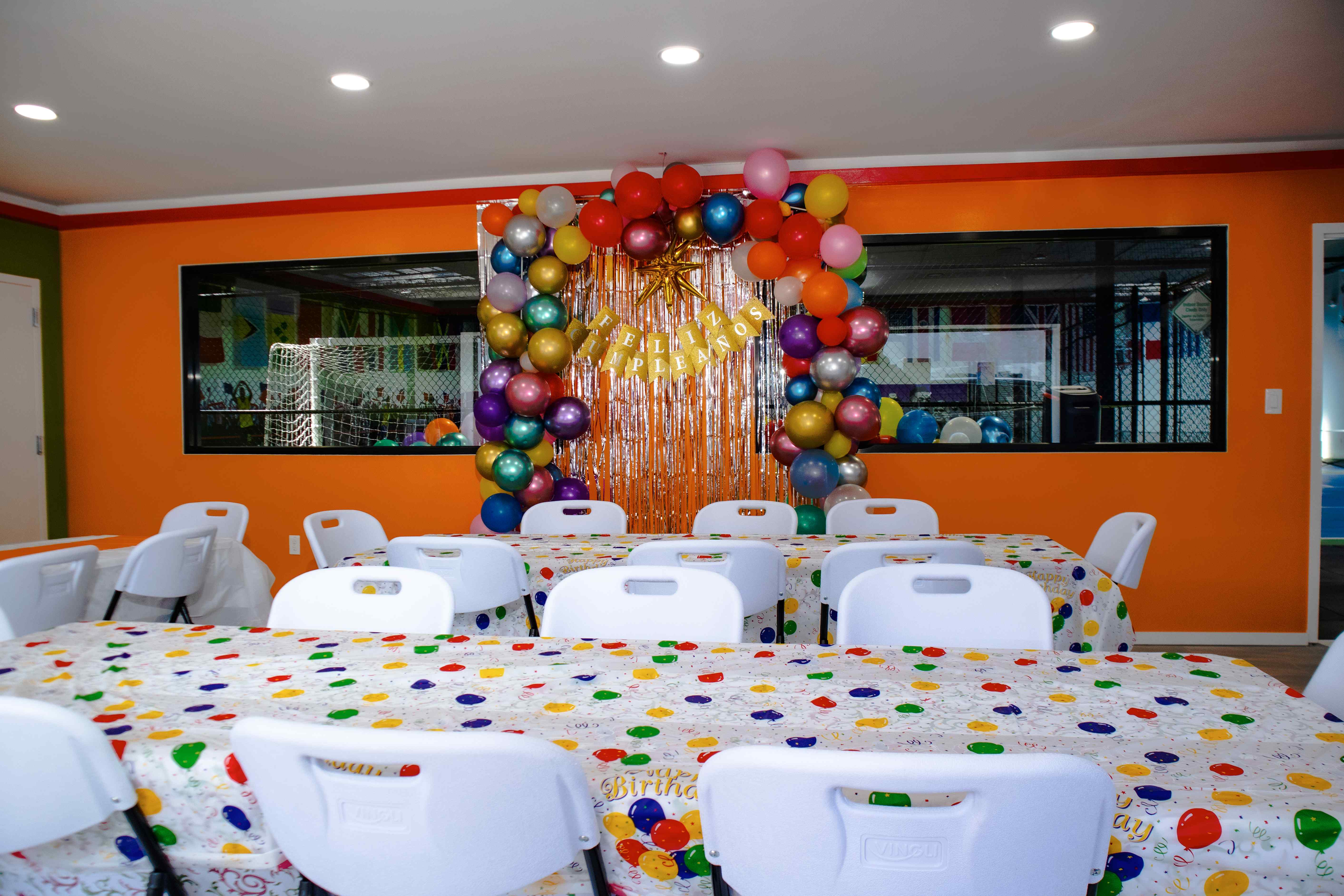 Birthday room with a Feliz Cumpleanos balloon arch and festive balloon-print tables