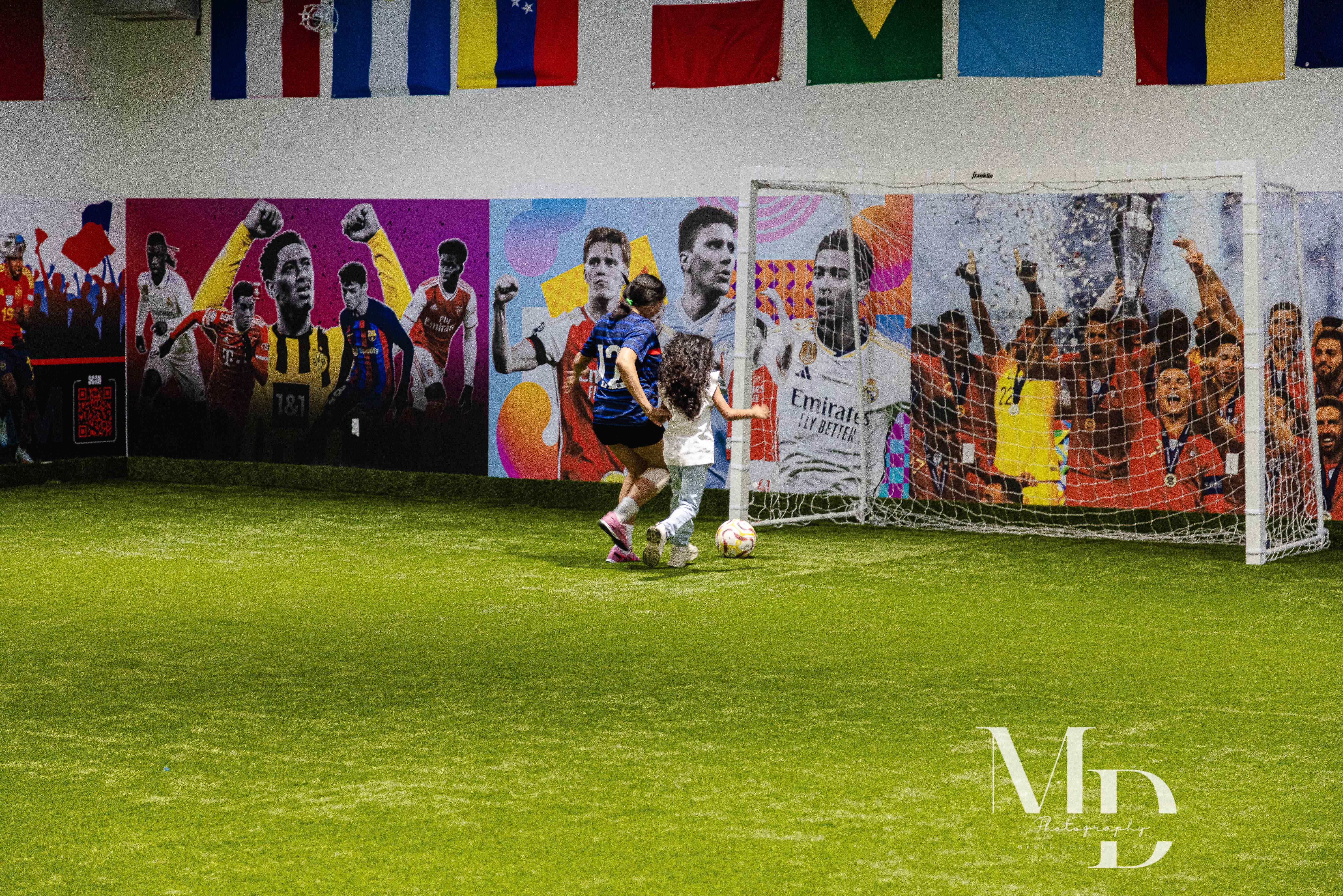 Kids playing soccer on the indoor turf field with a vibrant soccer mural
