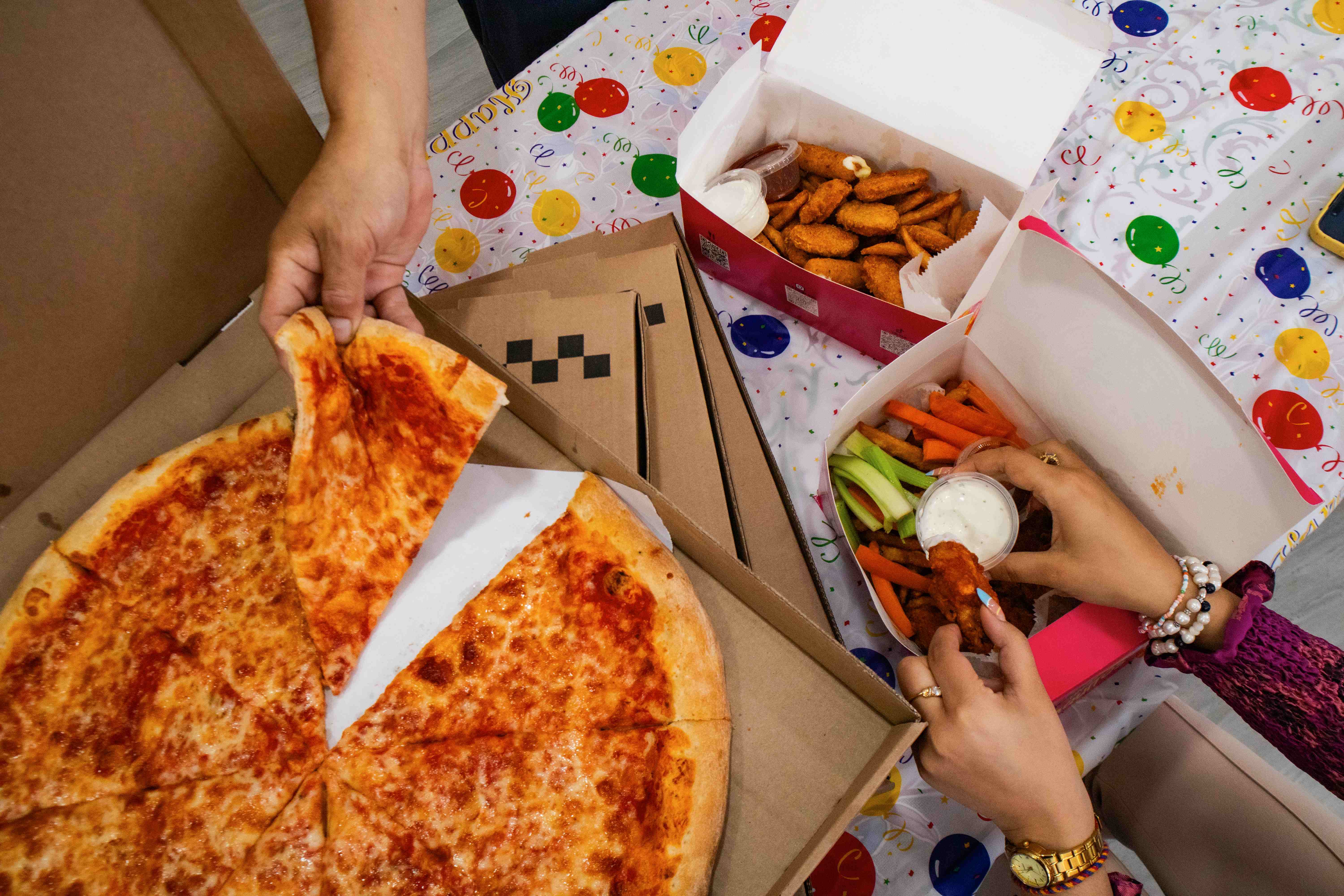 Party food spread with cheese pizza, chicken nuggets, fries, veggies, and wings