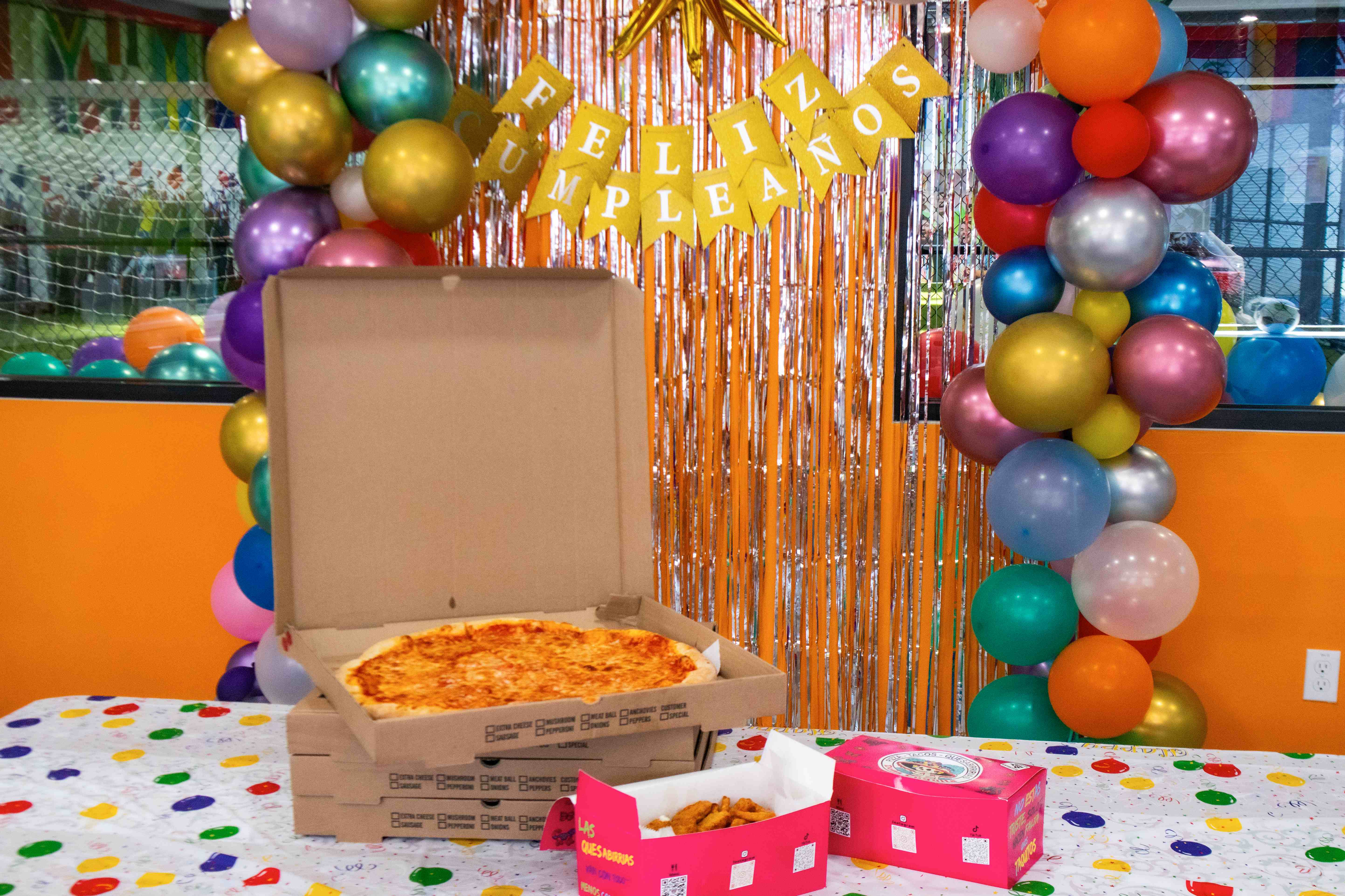 Open pizza box and nuggets on a table in front of a colorful balloon arch