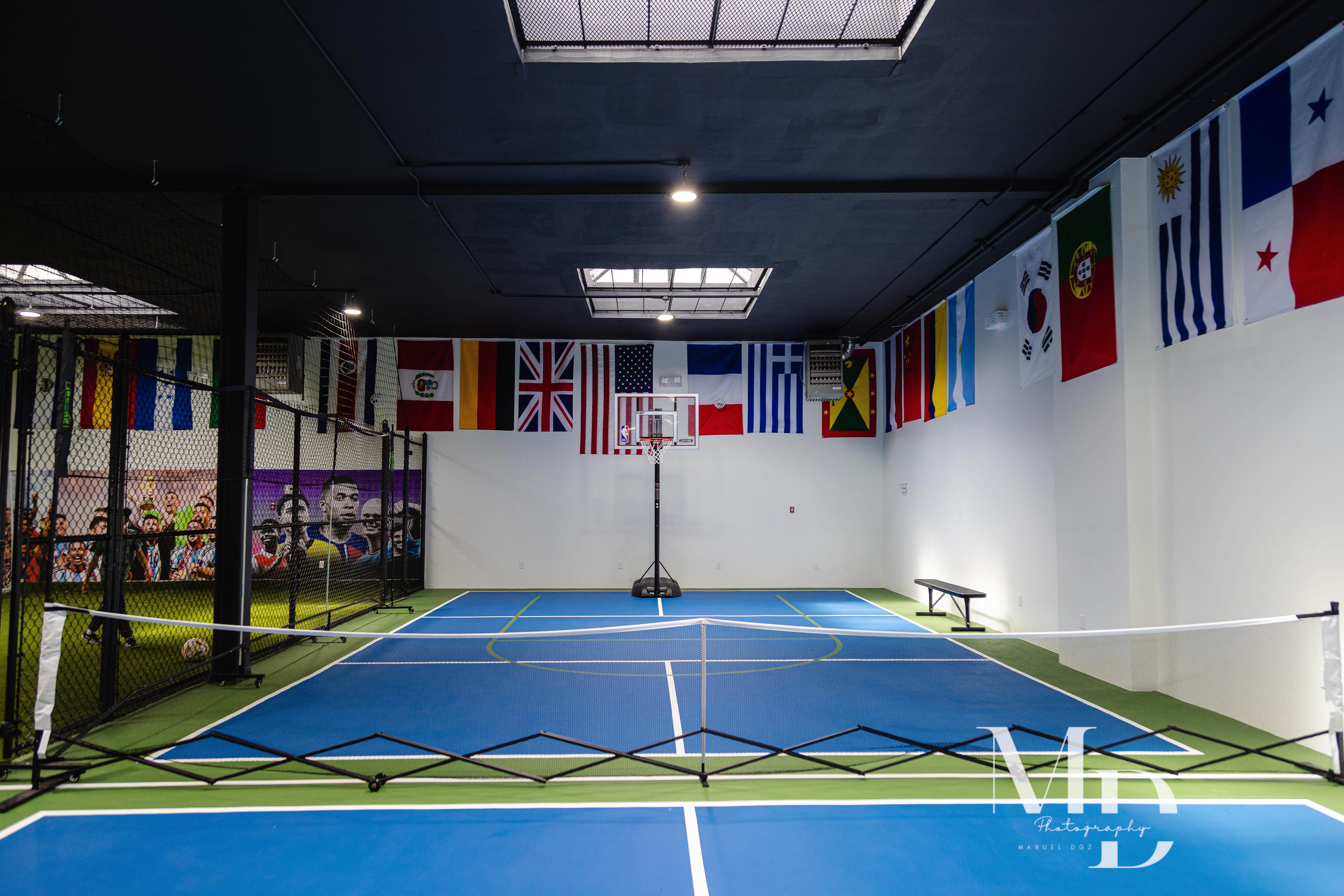 Indoor pickleball court with basketball hoop and international flags