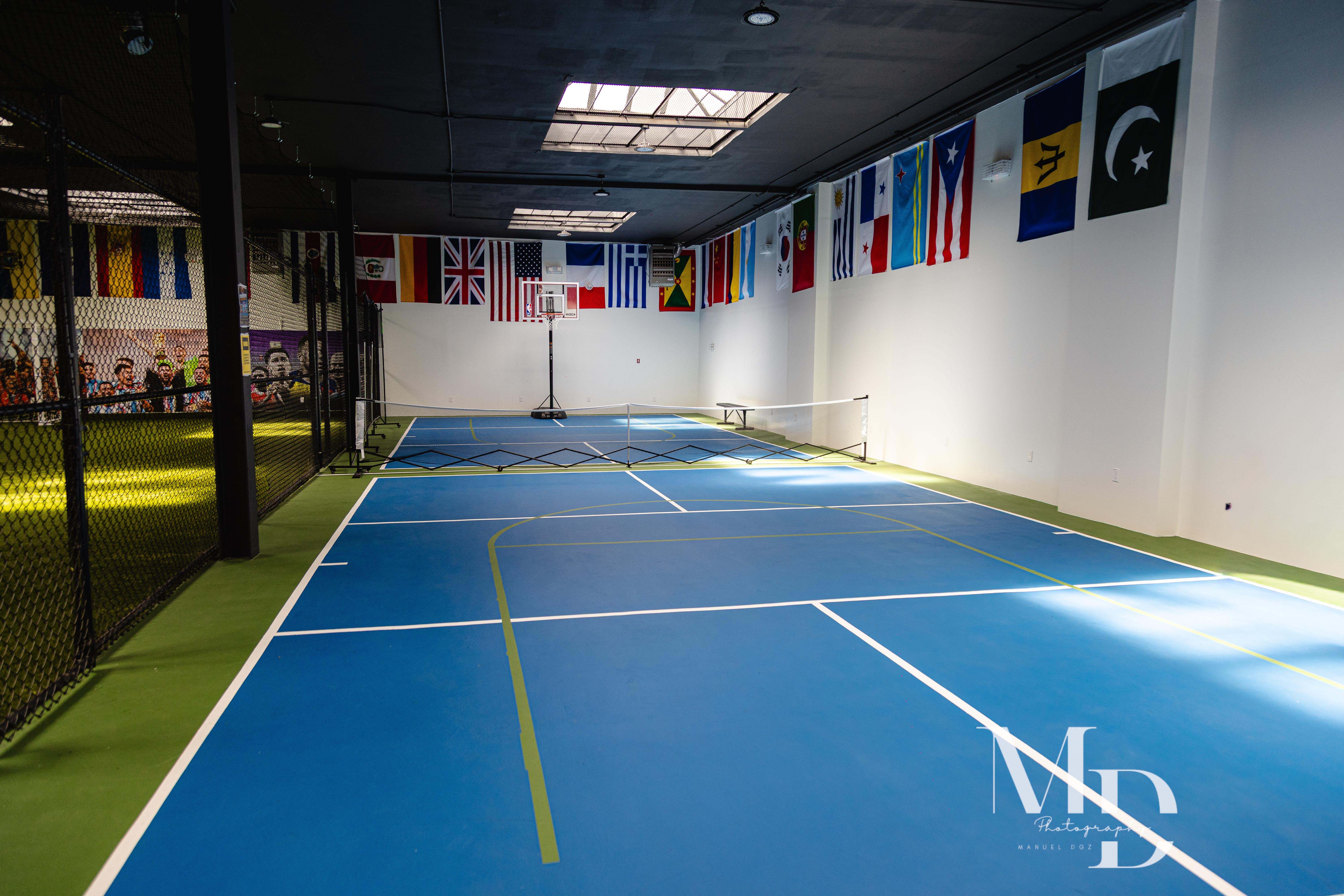 Wide view of the blue pickleball court lined with international flags